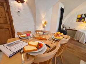 A dining table set with bread, fruit, and wine glasses, surrounded by wooden chairs in a room with white walls and a wooden door. - Charming apartment in Vars - 6 guests (Vars)