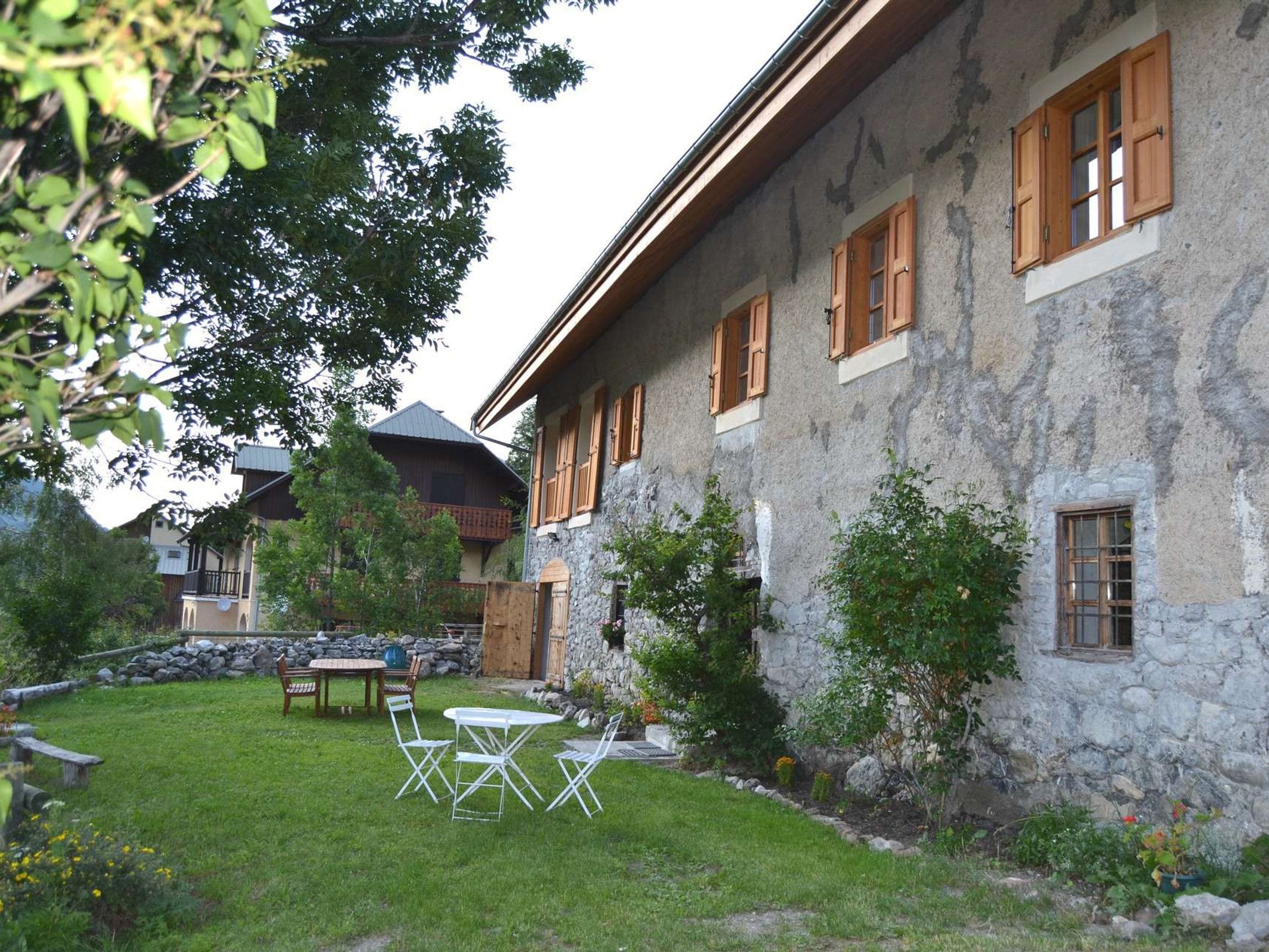 A stone building with wooden shutters, a grassy yard with outdoor furniture, and a stone wall.