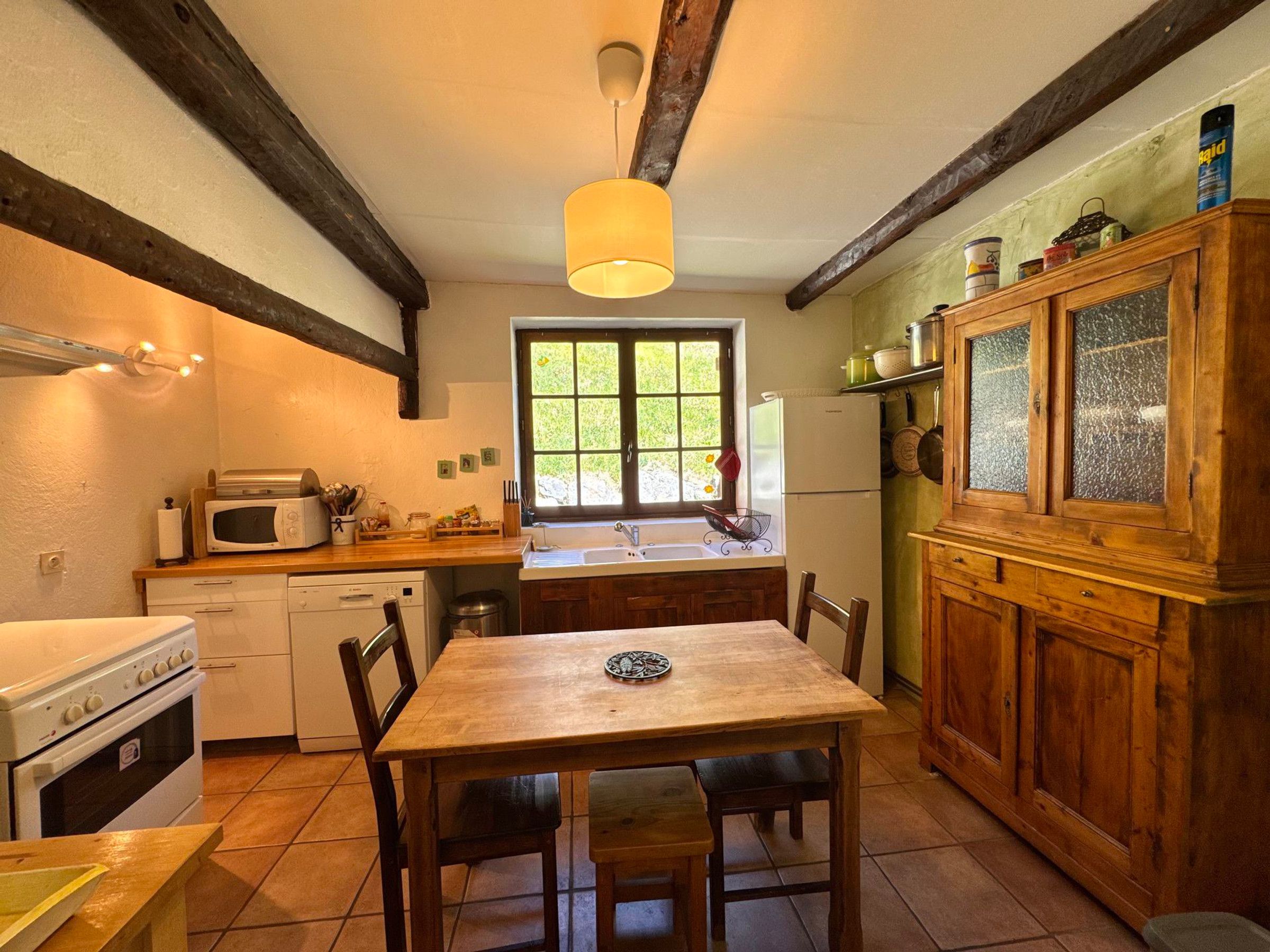 Cocina compacta con mesa de madera, microondas, refrigerador y ventana con vista a zonas verdes.