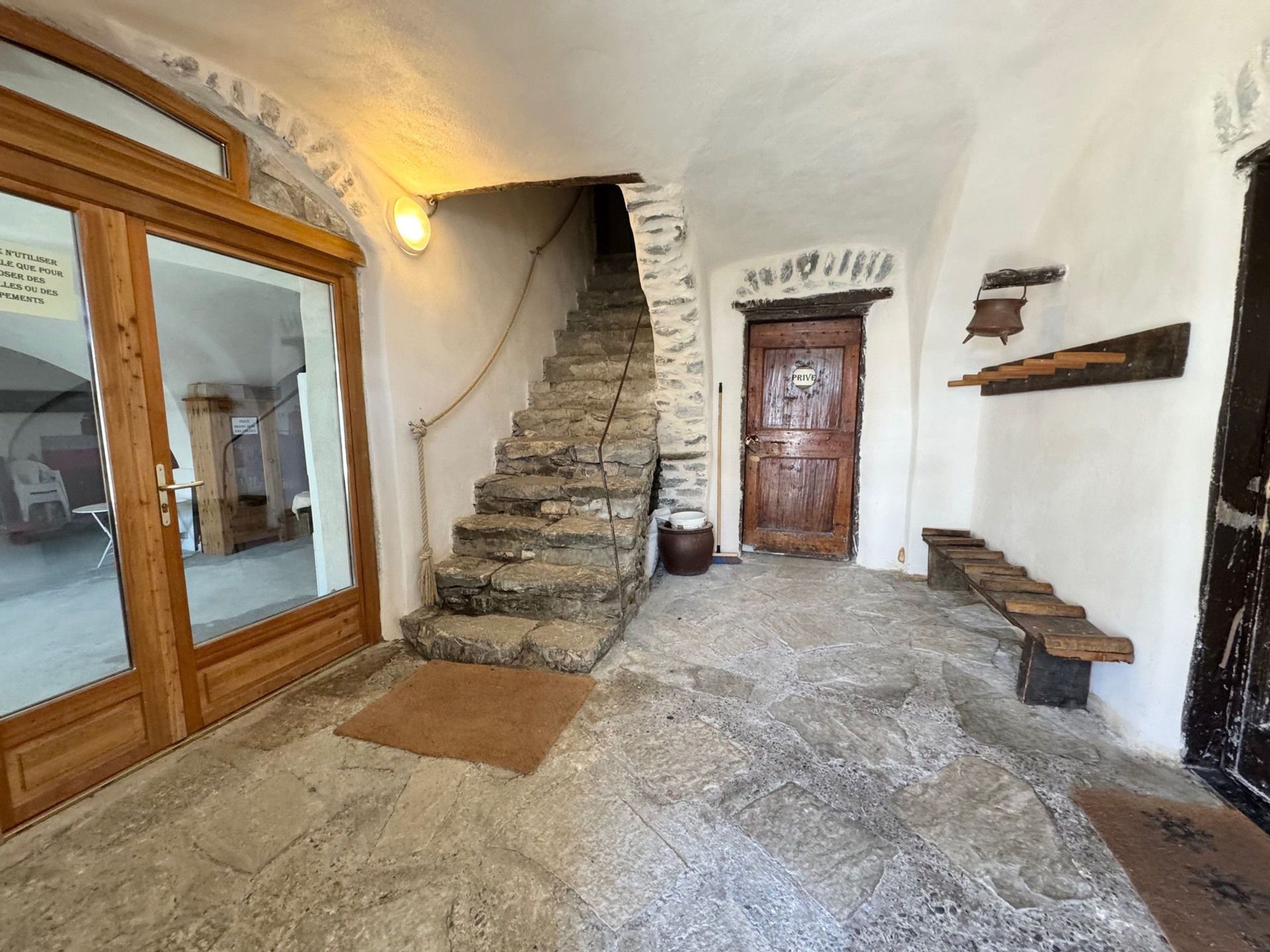 Eine Steintreppe führt zu einer Tür, die mit 'PRIVE' beschriftet ist, ein hölzerner Türrahmen und eine Steinmauer.