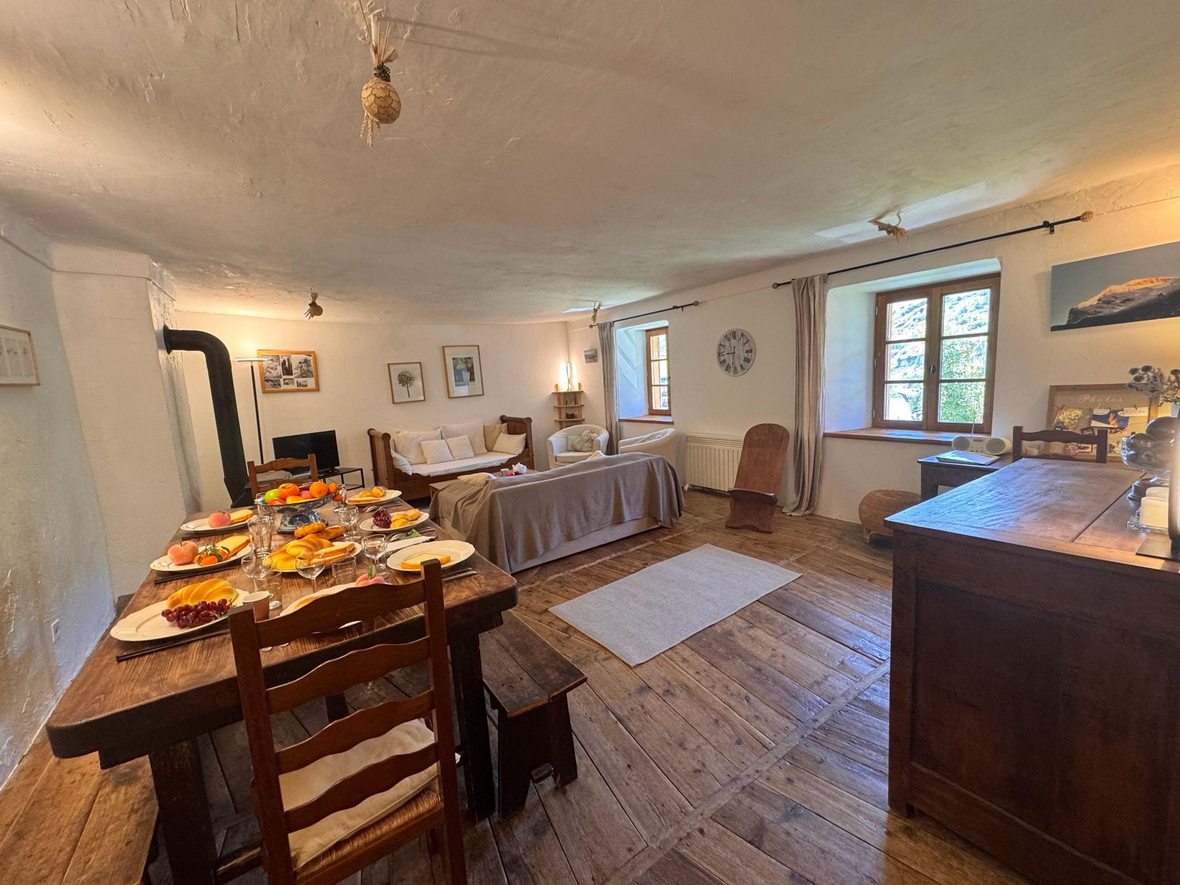A dining area with a wooden table set for a meal, a sofa, and a window with curtains.