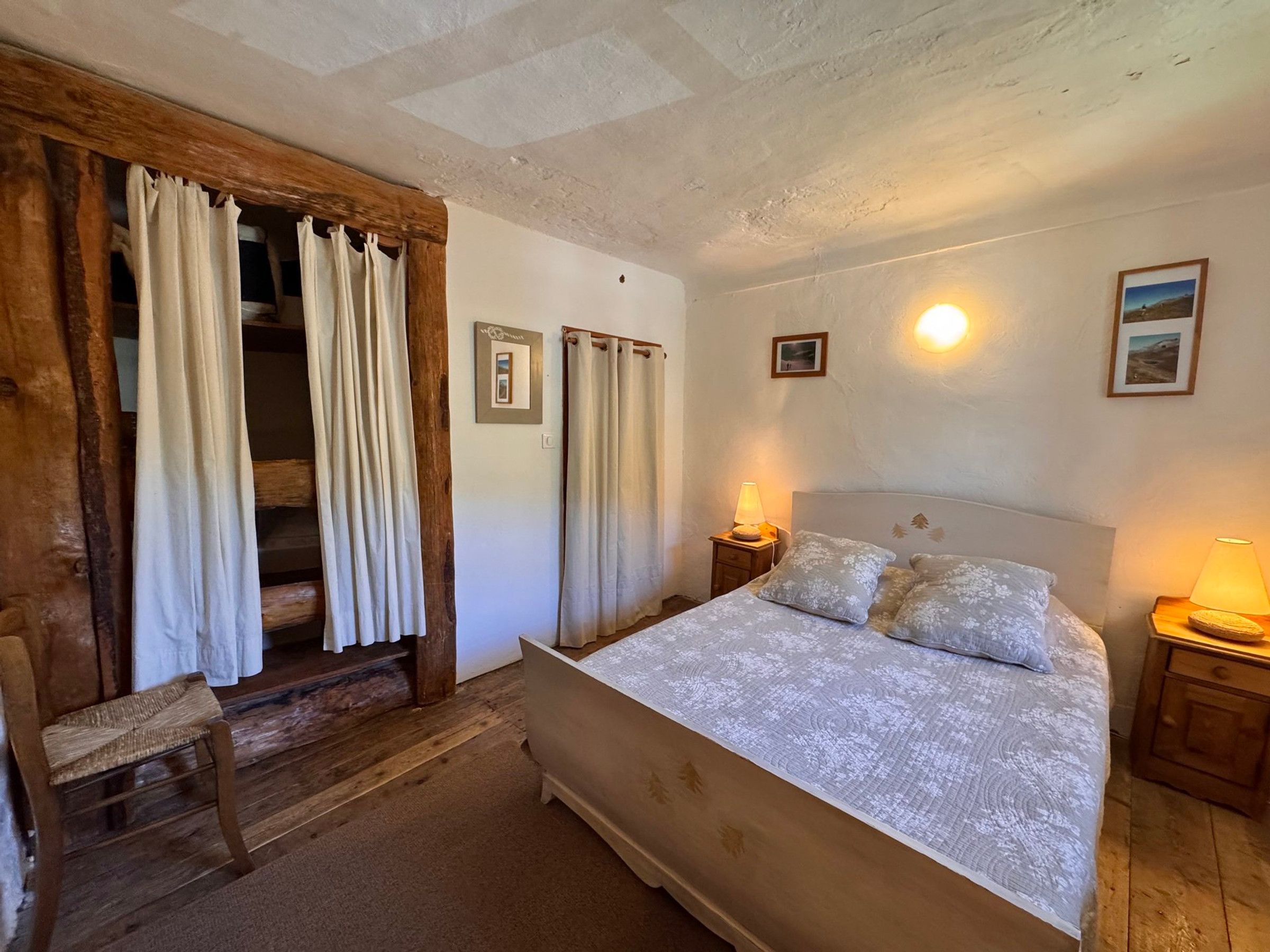 A bedroom with a bed, two bedside lamps, a chair, and a wooden bench.