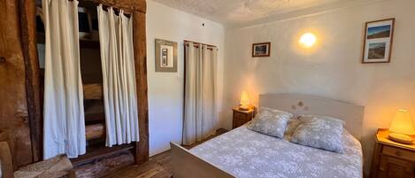 A bedroom with a bed, two bedside lamps, a chair, and a wooden bench.
