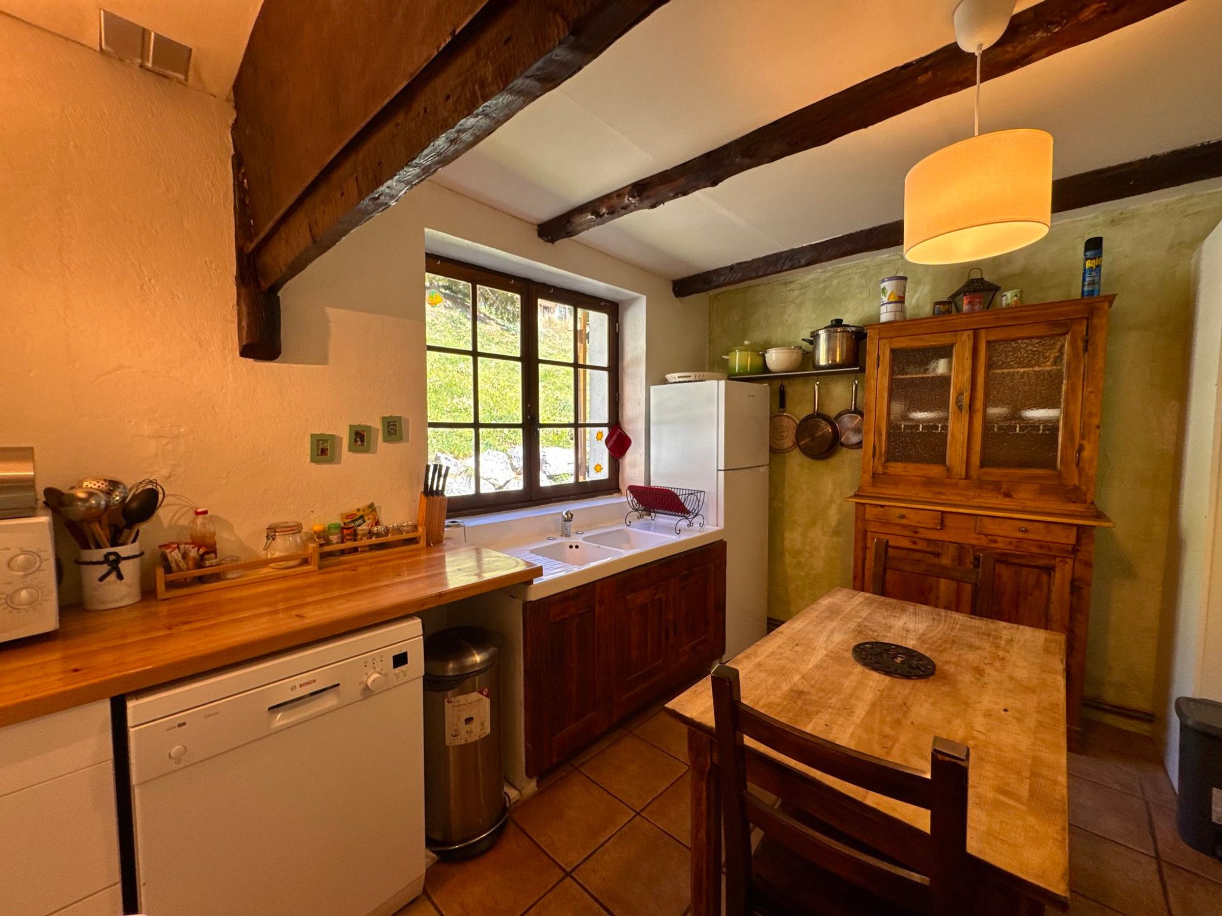A kitchen with a wooden countertop, a sink, a dishwasher, and a window with a view of greenery.