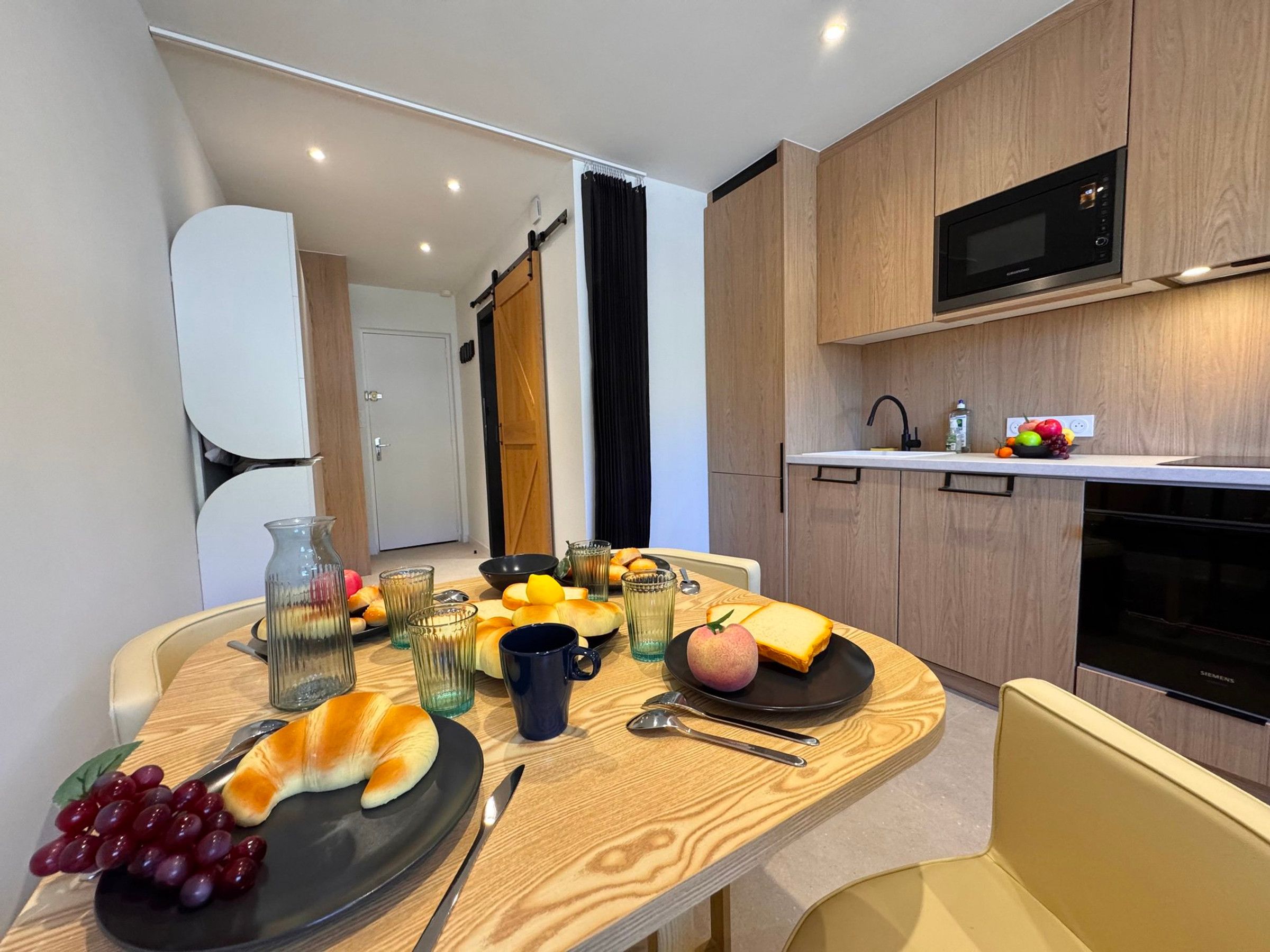 Una cocina moderna con armarios de madera, un microondas y un comedor con una mesa dispuesta para el desayuno.