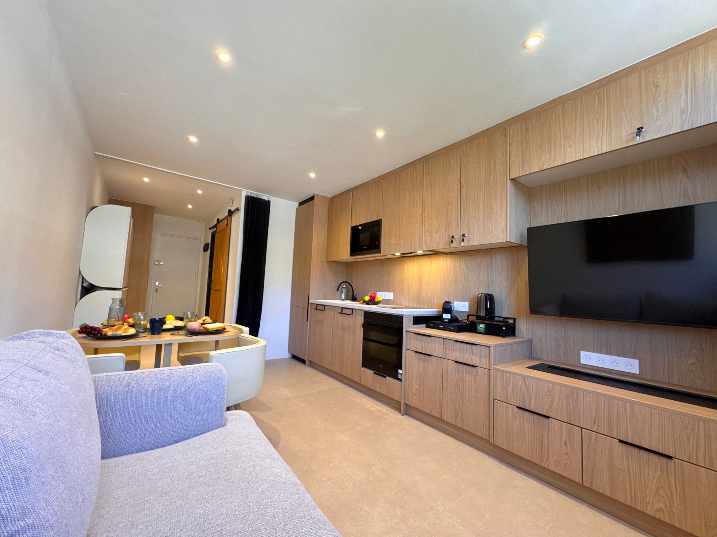 Een moderne keuken met houten kastjes, een inbouwmagnetron en een grote flatscreen televisie.