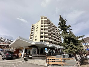 A multi-story hotel with a modern design, featuring a prominent entrance and a parking area in front. - Apartment in the heart of Vars - 4 guests (Vars)