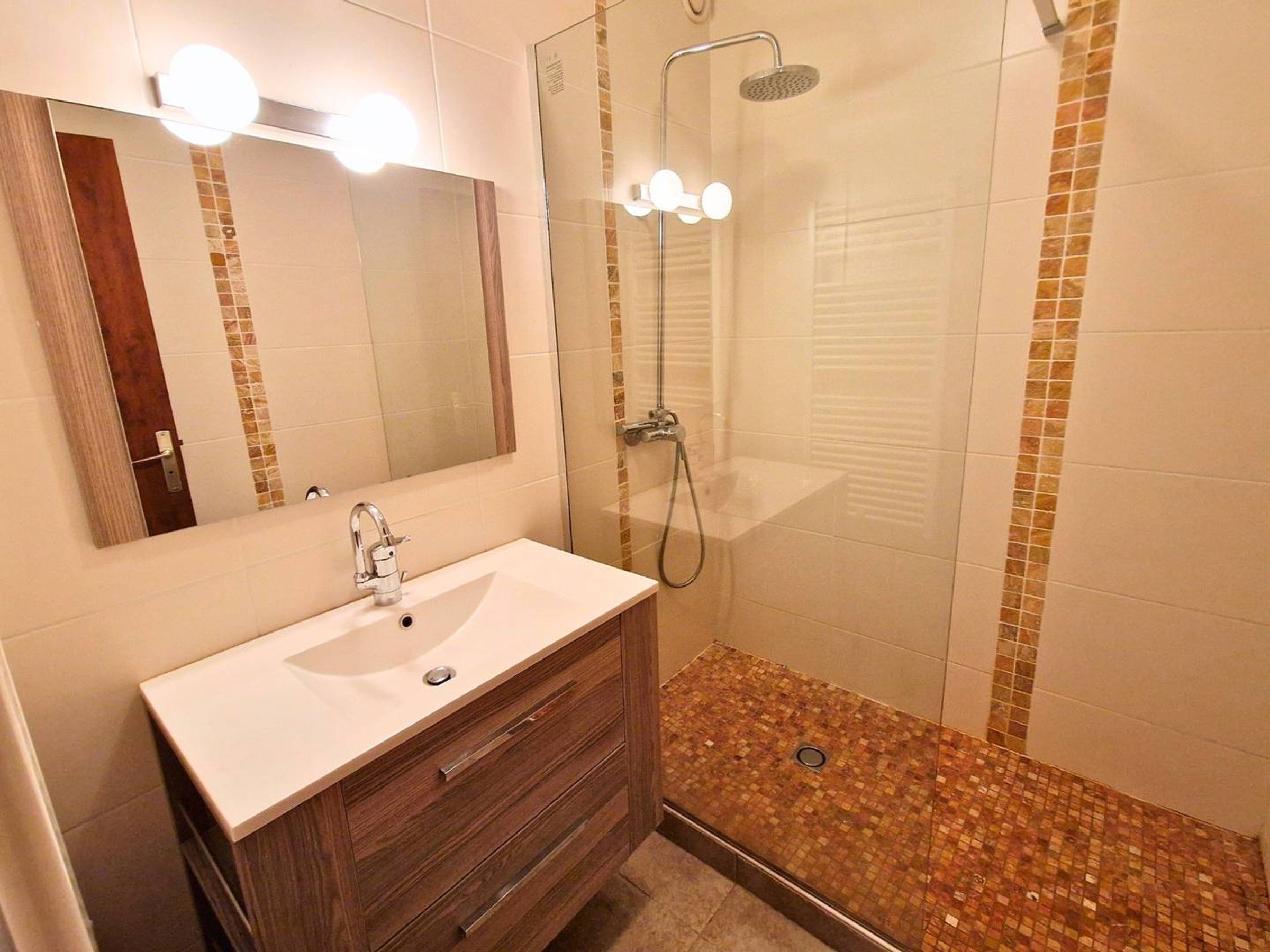 A bathroom with a sink, mirror, and shower.