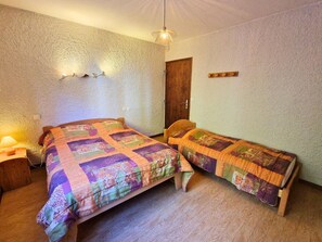 Une petite pièce chaleureuse avec deux lits en bois, une porte en bois et un mur à la texture particulière.