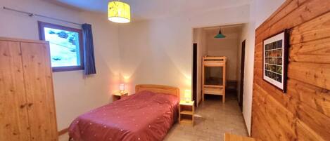 Een slaapkamer met een bed, nachtlampjes, een houten garderobe, een raam met gordijnen en een houten wand met een lijstwerk.