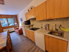 Een kleine keuken met houten kastjes, een magnetron, een koffiezetapparaat en een spoelbak.