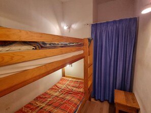 Een kleine accommodatie met één kamer, voorzien van een stapelbed en een enkel bed.