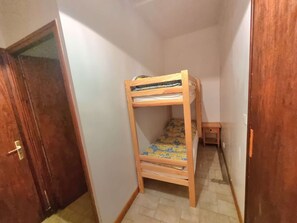 Een kleine, smalle kamer met een houten stapelbed, een klein houten tafeltje en een deur.