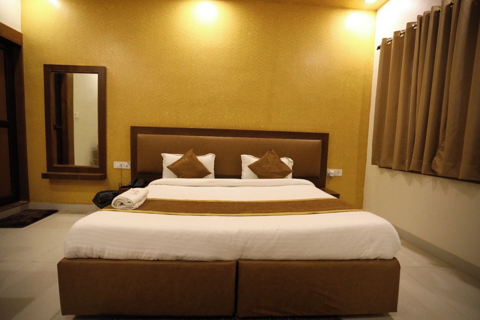 A hotel room with a large bed, a bedside table, a mirror, and a curtain.