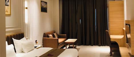 A hotel room with a bed, a sofa, a desk, a chair, a TV, and a ceiling fan.