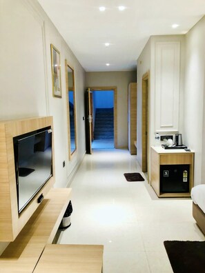 A hotel room with a flat-screen TV, a wooden cabinet, a small desk, a bed, and a bathroom with a sink and mirror.