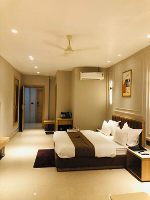 A hotel room with a large bed, bedside tables, an air conditioning unit, a ceiling fan, and a door leading to another room. - BLISS Resort (Bahraich)