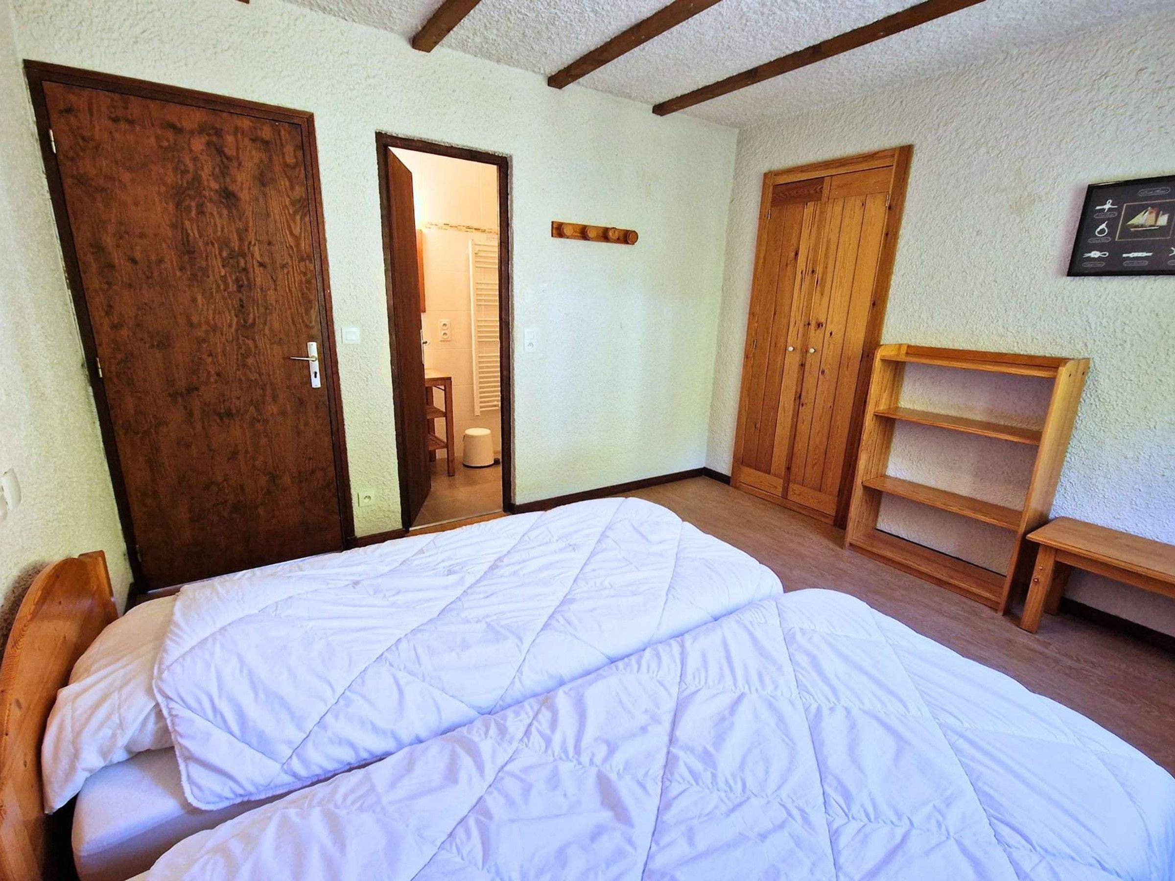 Een kamer met een bed, een houten garderobe en een klein houten plankje.