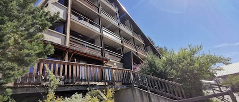 Un immeuble à plusieurs étages doté de balcons, d’un escalier en bois et entouré de verdure.