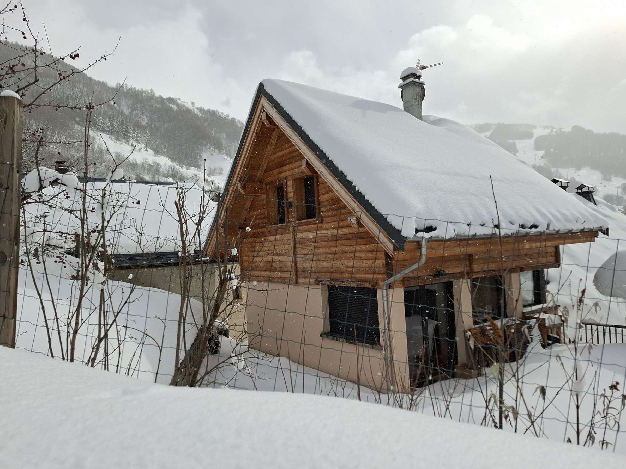 Una cabaña de madera con techo nevado, rodeada por un paisaje invernal y montañas.