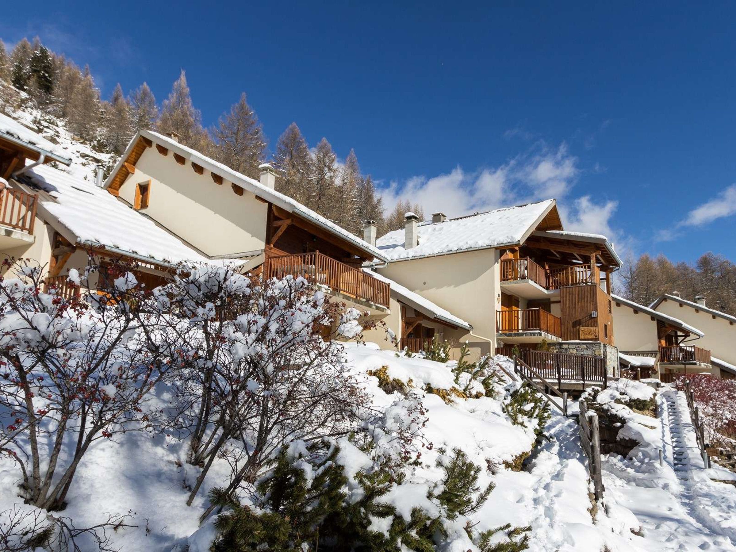 Un bâtiment de style chalet, doté de nombreux balcons, entouré d’arbres couverts de neige et surplombant un ciel dégagé.