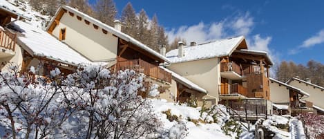 Un bâtiment de style chalet, doté de nombreux balcons, entouré d’arbres couverts de neige et surplombant un ciel dégagé.