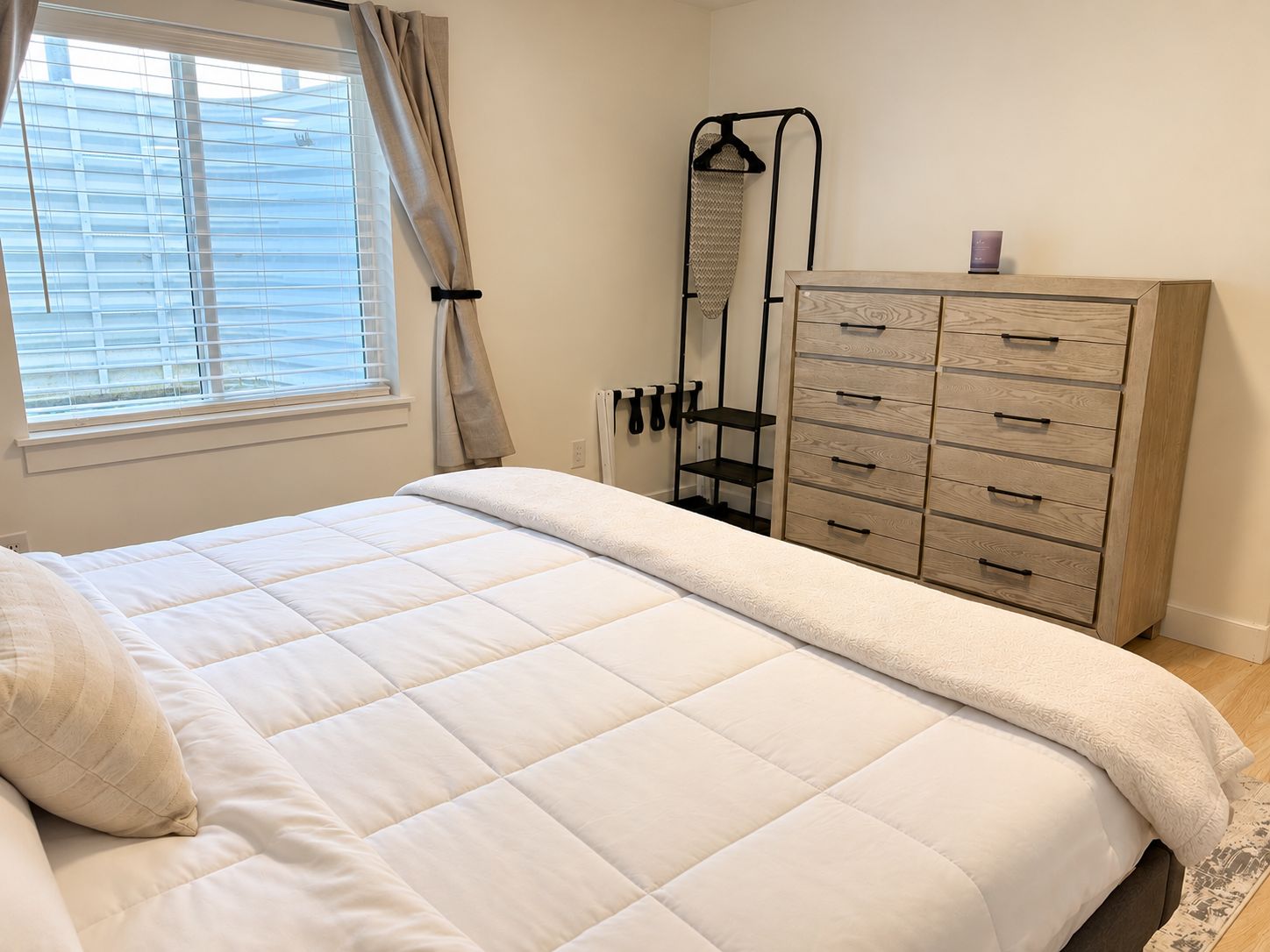 Une chambre à coucher avec un lit, une commode, un radiateur et une fenêtre avec des rideaux.