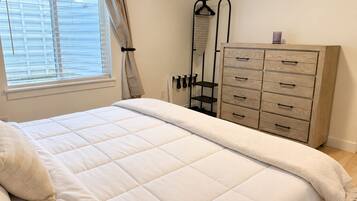 Une chambre à coucher avec un lit, une commode, un radiateur et une fenêtre avec des rideaux.