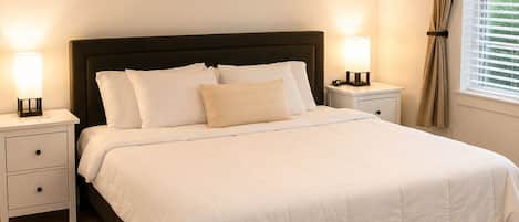 Un dormitorio con cama, mesitas de noche, una alfombra y una ventana con cortinas.