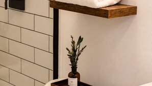 Une salle de bain avec des toilettes, une douche et un lavabo. On y trouve un porte-serviettes avec des serviettes pliées et une petite plante posée sur un plateau.