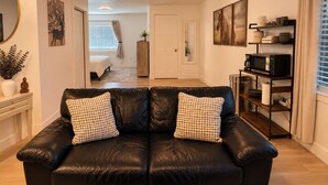 Un salon comprenant un canapé en cuir noir, une table basse, une bibliothèque et un coin repas avec une table et des chaises.