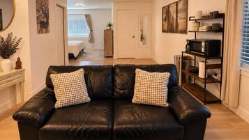 Een woonkamer met een zwarte leren bank, een bijzettafeltje, een boekenkast en een eethoek met tafel en stoelen.