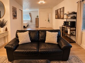 A living room with a black leather sofa, a coffee table, a bookshelf, and a dining area with a table and chairs.