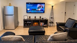 Un salon moderne avec un téléviseur à écran plat fixé au mur, un meuble de rangement en bois foncé en dessous, un canapé en cuir noir, une petite table agrémentée d’objets décoratifs et un lampadaire.