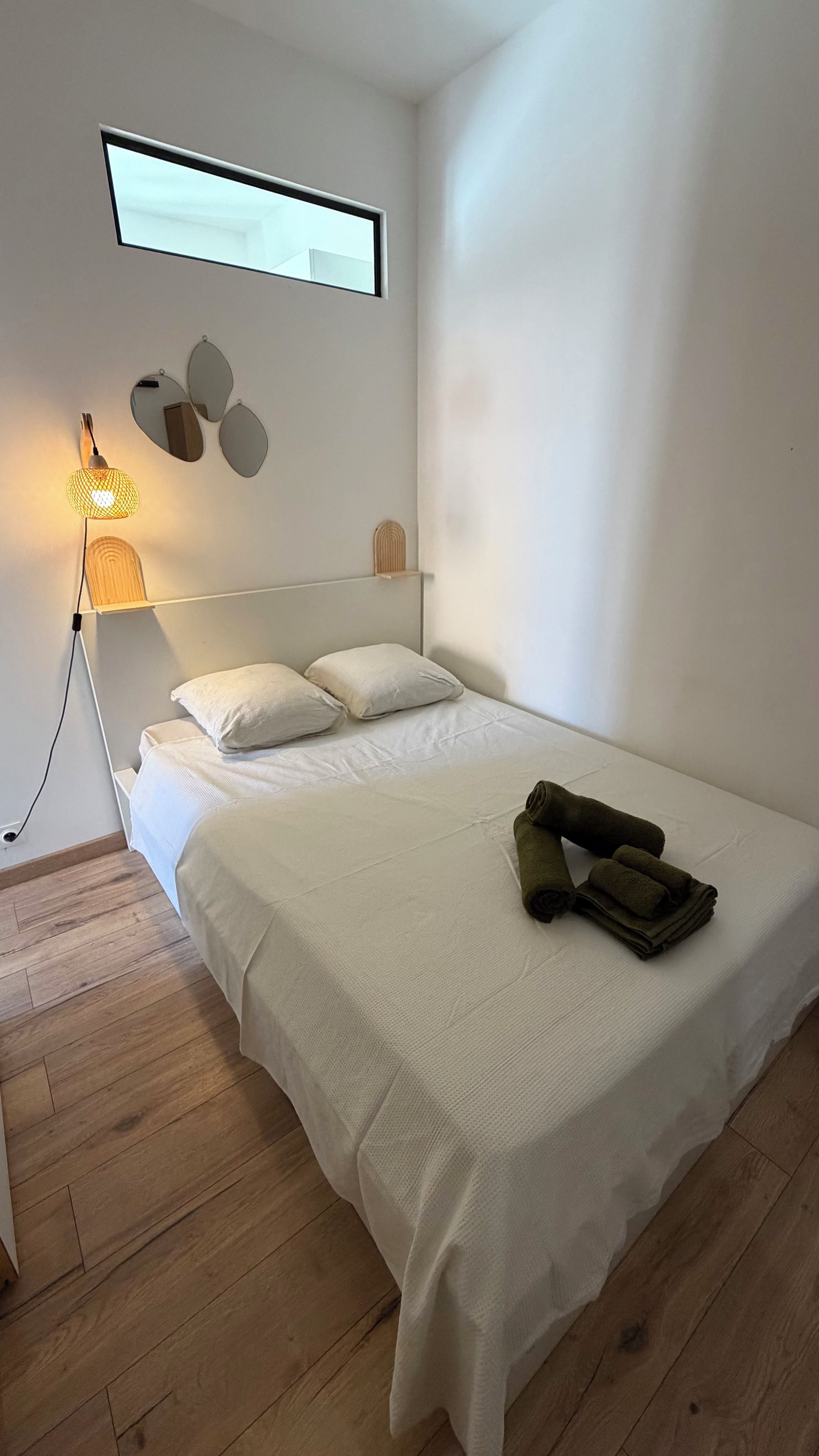Ein modernes Schlafzimmer mit einem Bett, einer Nachttischlampe und einem wandmontierten Spiegel.