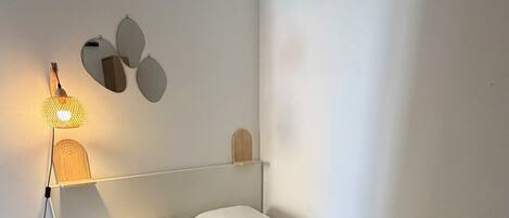 Une chambre à coucher moderne avec un lit, une lampe de chevet et un miroir fixé au mur.