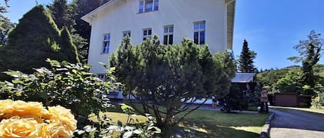A two-story building with a flat roof, surrounded by a well-maintained lawn and a variety of trees.