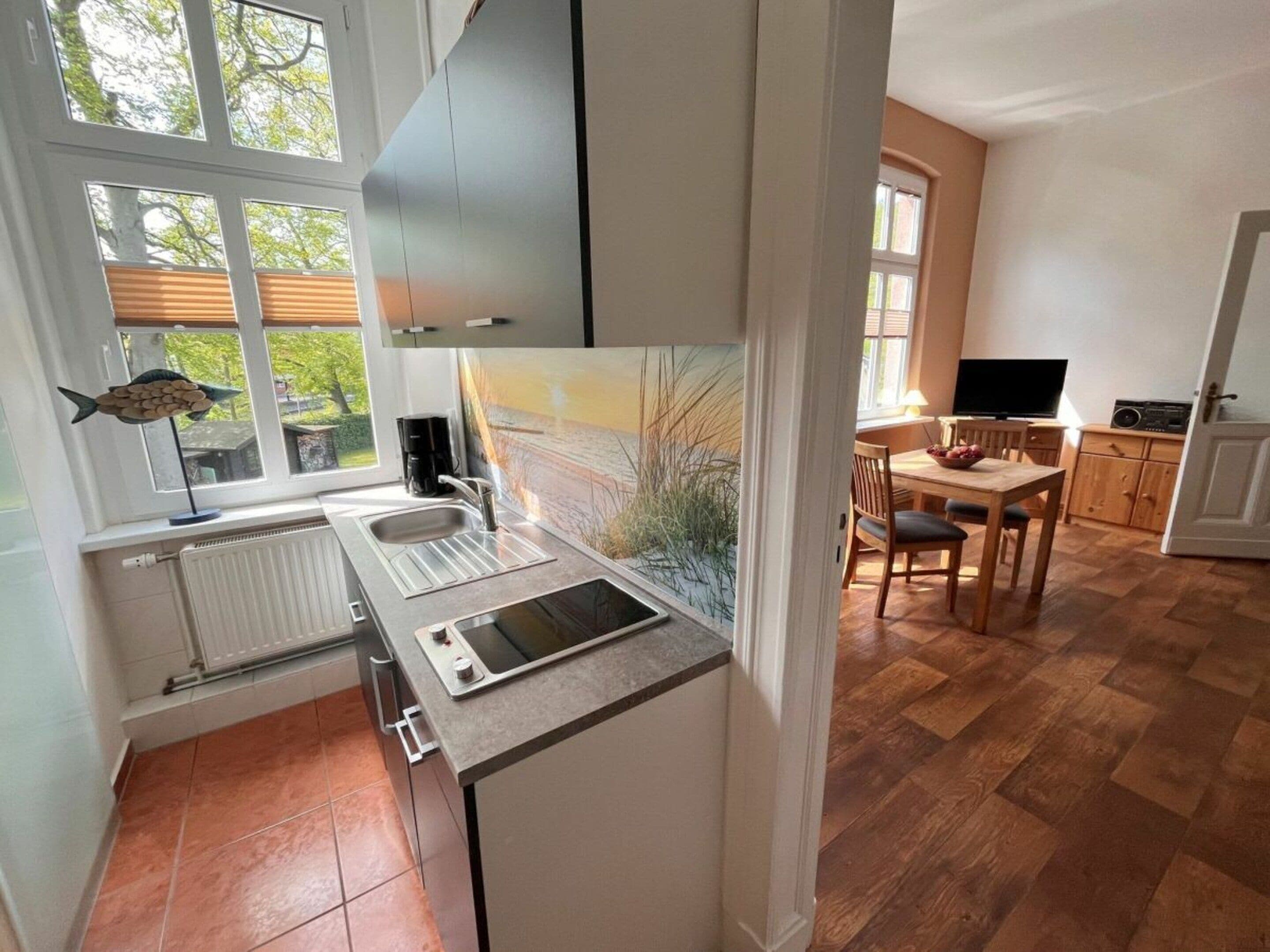 A modern kitchen with a built-in stove, a sink, and a window overlooking a garden.