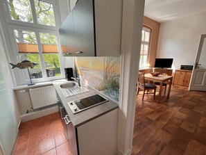 A modern kitchen with a built-in stove, a sink, and a window overlooking a garden. - Fiedler Holiday Apartments (Heringsdorf)
