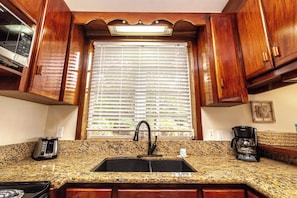 A kitchen with a granite countertop, a black faucet, wooden cabinets, a window with blinds, and a coffee maker. - Seahorse | Oceanfront Couples Escape (San Pedro Town)