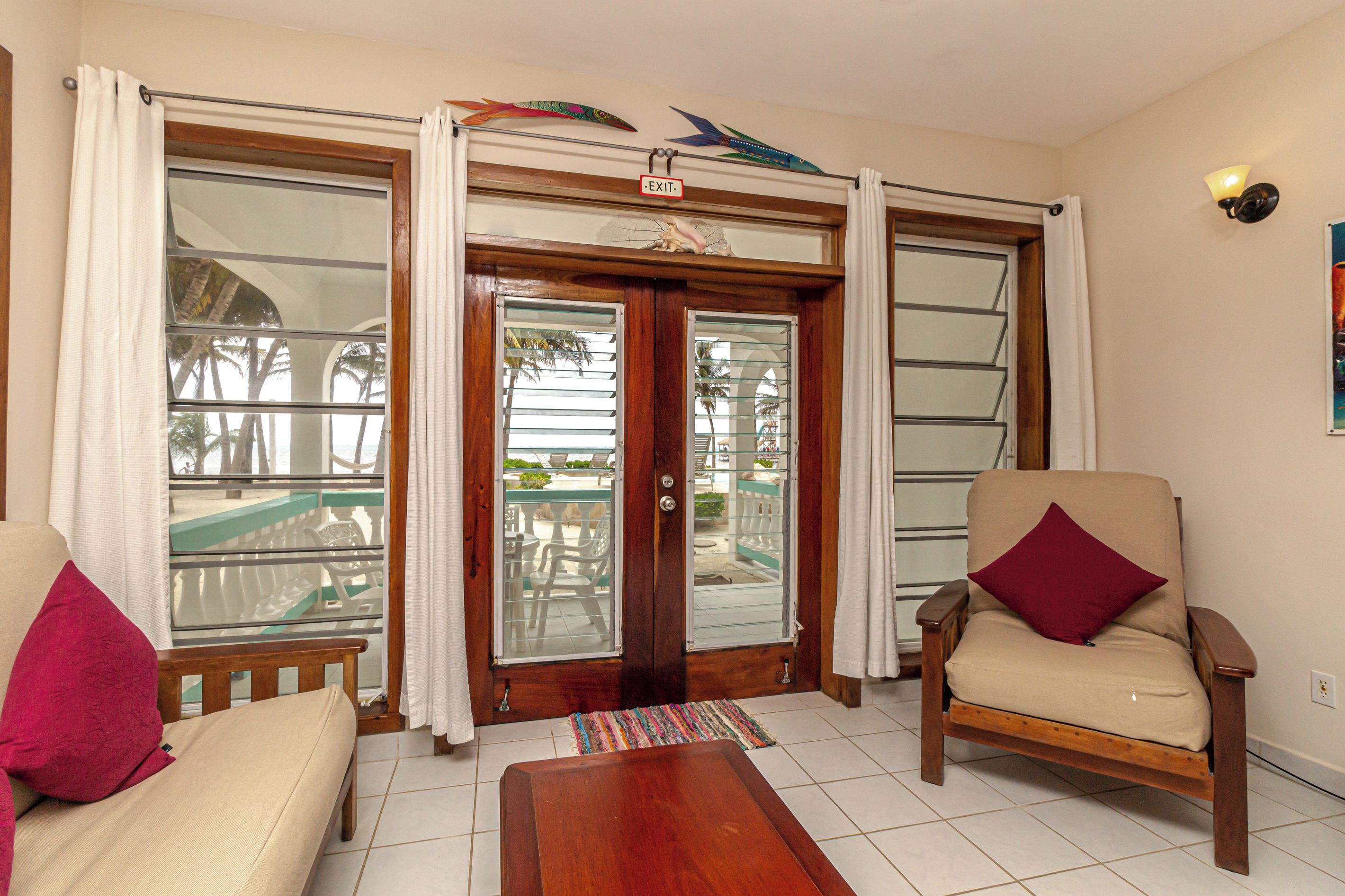 A room with a wooden door, a bench, a chair, and a view of the outdoors through the door.