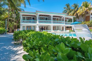 A two-story building with a pool, surrounded by greenery and palm trees. - Seahorse | Oceanfront Couples Escape (San Pedro Town)