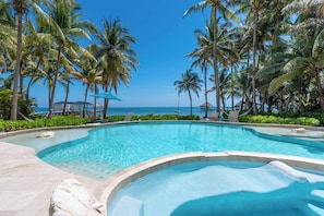 A clear blue pool surrounded by palm trees, with a view of the ocean and a beach in the background. - Seahorse | Oceanfront Couples Escape (San Pedro Town)