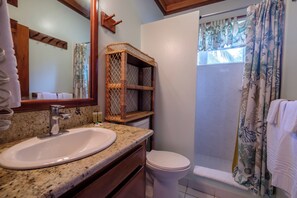 Ein Badezimmer mit Marmorwaschtisch, einem Holzregal, einer Toilette und einer Dusche mit gemusterten Vorhängen.