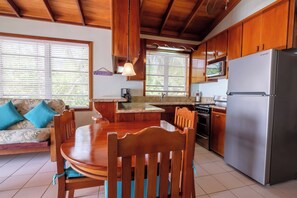 Une cuisine avec des meubles en bois, un réfrigérateur en acier inoxydable, une table à manger avec des chaises et une fenêtre avec des stores.