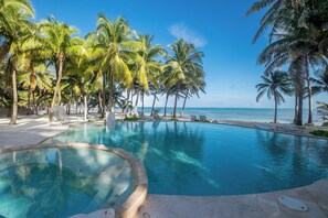Ein Pool mit klarem, blauem Wasser, umgeben von Palmen und Blick auf den Ozean.