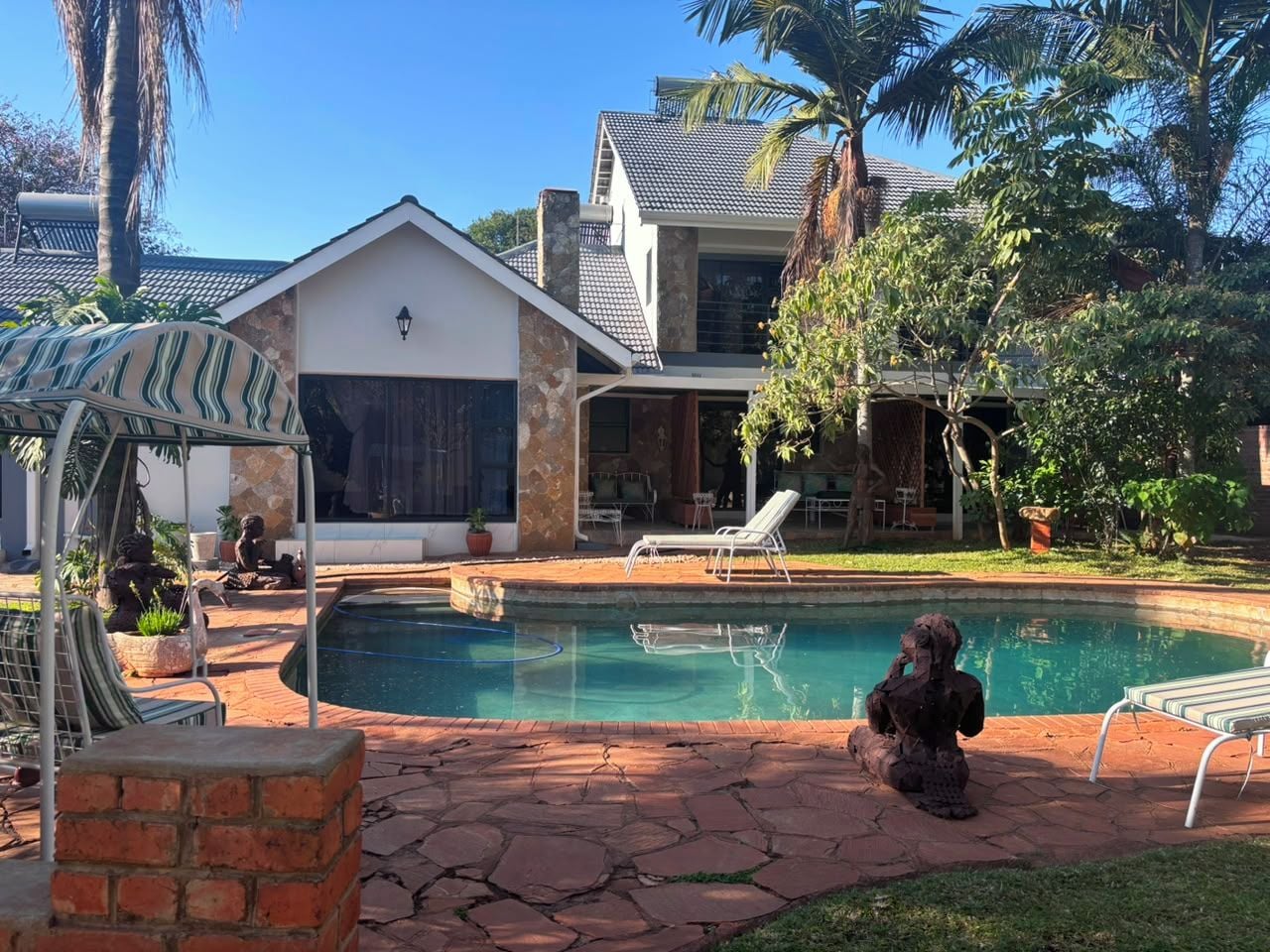 Ein Garten mit Swimmingpool, einer überdachten Terrasse und einem Haus mit Ziegeldach.