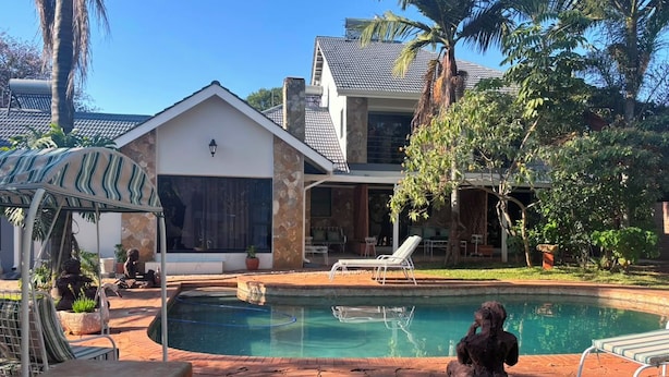 A backyard with a swimming pool, a covered patio, and a house with a tiled roof. - On Guest Av (Harare)
