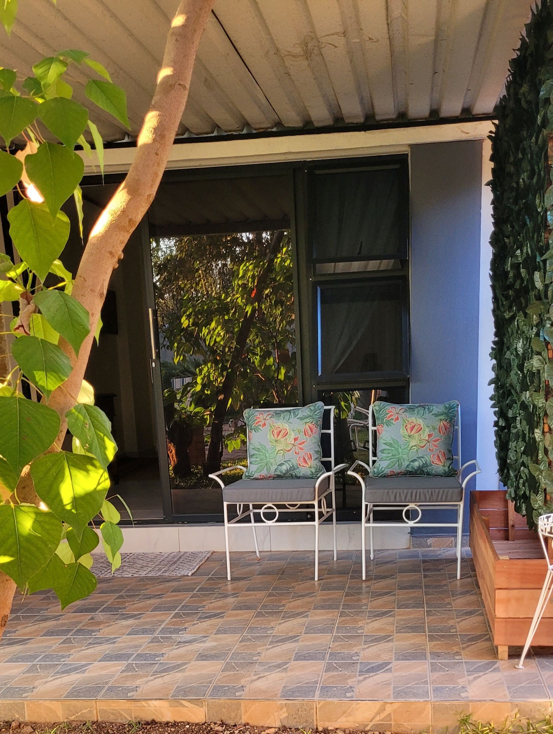 Un espace extérieur abrité, aménagé avec un banc et une table, entouré de plantes en pot et doté d’un sol carrelé.
