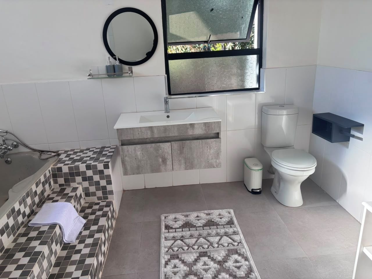 A bathroom with a checkered tile tub, a sink, a toilet, and a patterned rug.